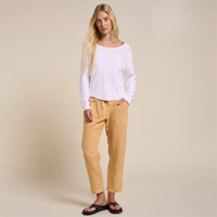 Woman wearing a white sweater and mustard linen pants on a beige background