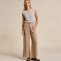 Woman wearing a striped sleeveless top and beige pants against a beige background