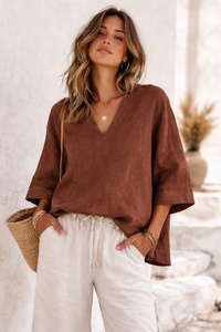 Woman wearing a brown top and white pants with a neutral background