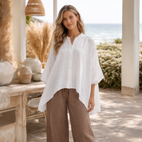 Woman wearing a white shirt and brown pants standing in a sunlit outdoor setting.
