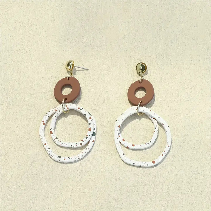 Pair of earrings with brown and white circular designs on a beige background