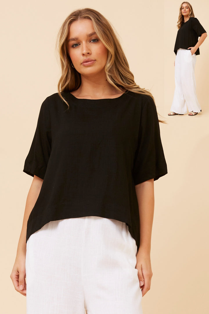 Woman wearing a black top and white pants on a beige background