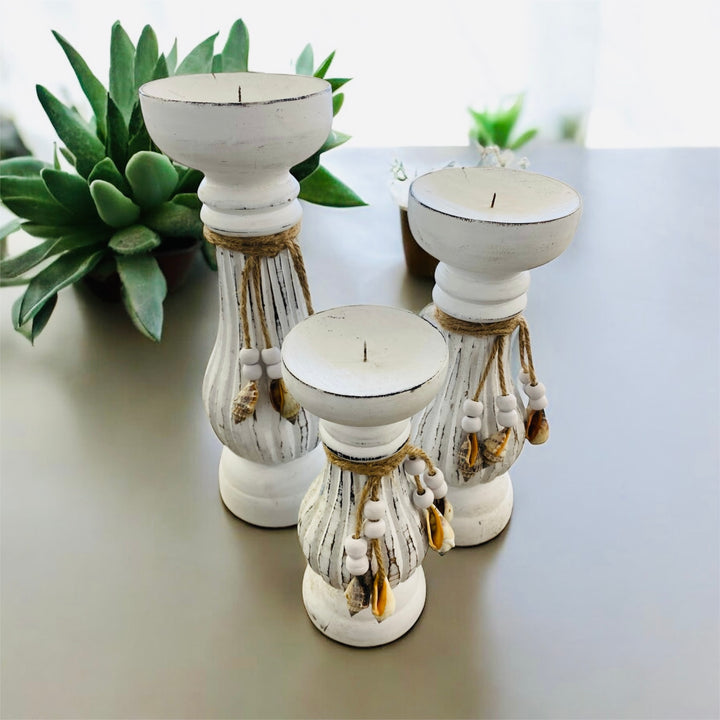 Set of three white wash pillar candle holders with decorative elements on a light surface.