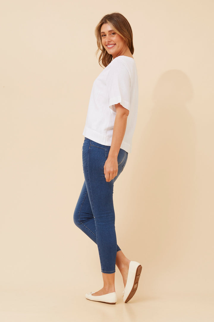 Woman wearing a white top and blue jeans on a beige background