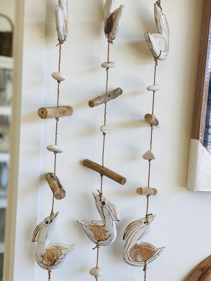 Decorative wall hanging with birds, stones, and driftwood on a white wall.
