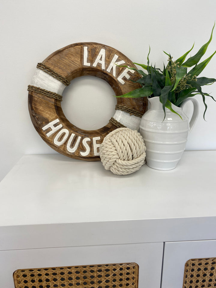 Decorative buoy with 'Lake House' text on a white surface with a plant and vase.