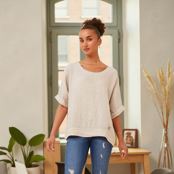 Close view of a natural linen top showing the cuffed sleeves and hem button detail.