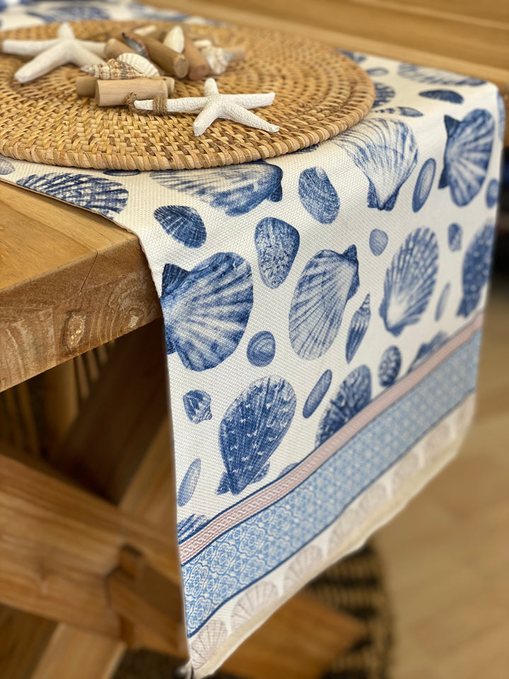 Coastal table runner with navy-blue seashell motif on a crisp white background, featuring decorative border and fringe detail, perfect to Hamptons or beach house styling