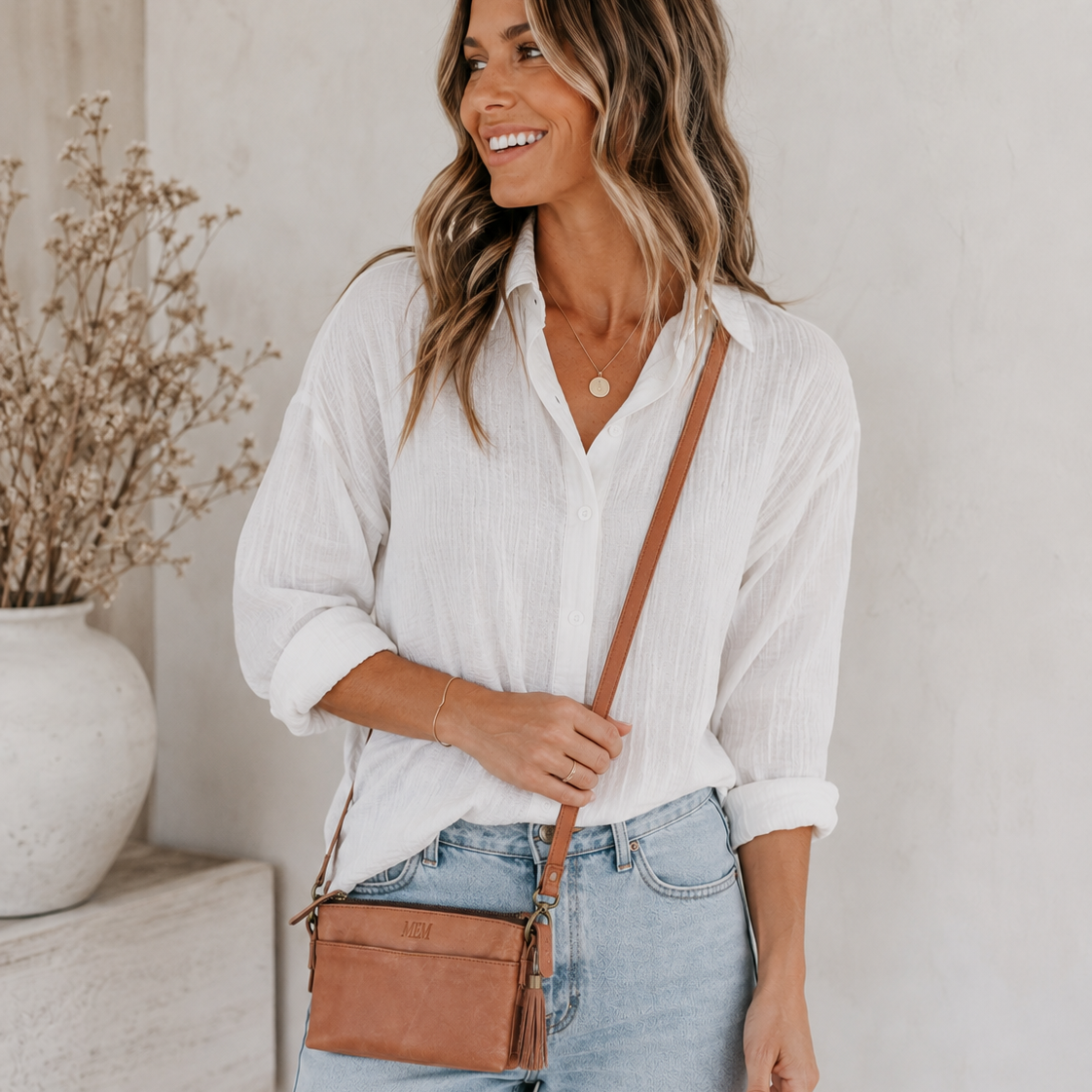 Woman in a white shirt and jeans wearing a brown leather crossbody bag
