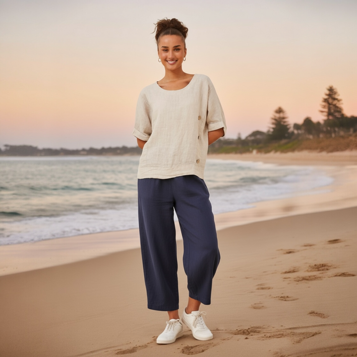 Woman wearing a natural-toned relaxed linen top with rolled sleeves and button detail at the hem