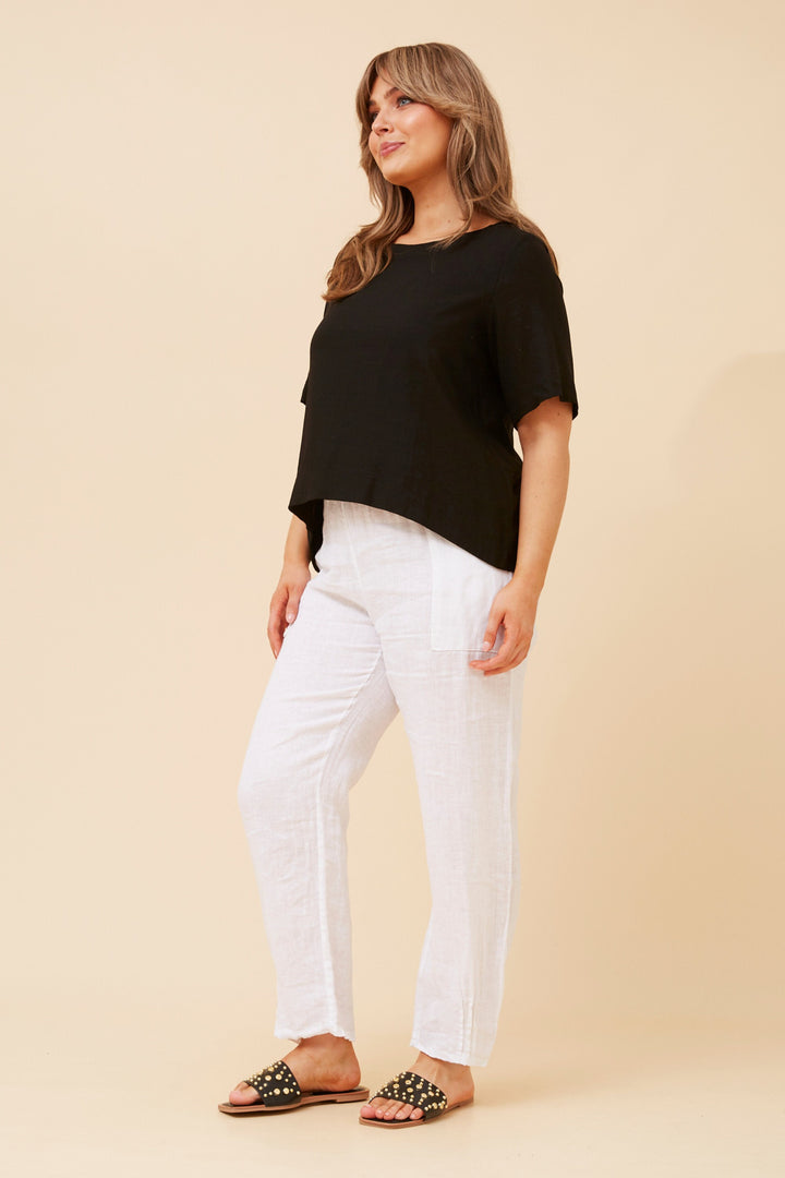 Woman wearing a black top and white pants on a beige background