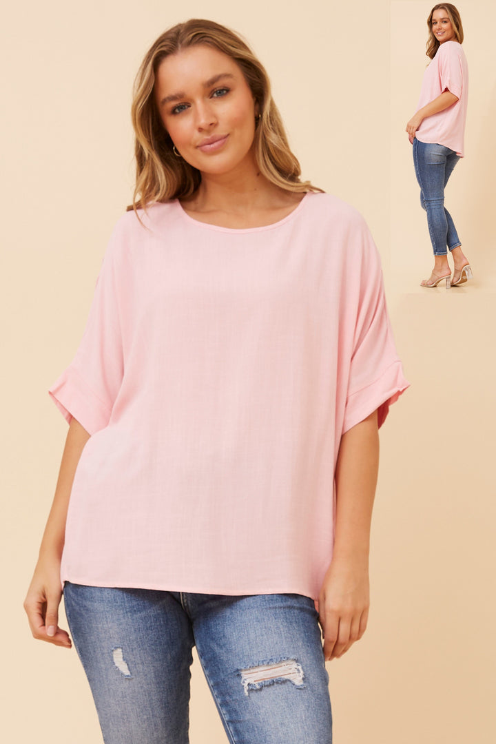 Woman wearing a pink oversized top and blue jeans on a beige background
