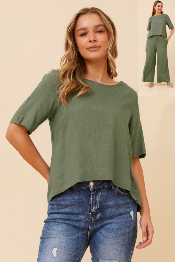 Woman wearing a green top and blue jeans on a beige background