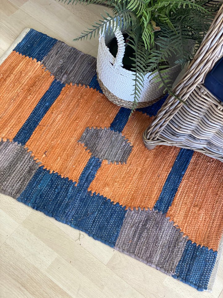Geometric patterned rug with blue and orange squares on a wooden floor.