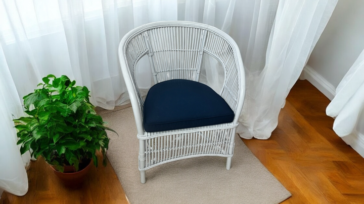 A white Bagas Slat Chair with a dark blue seat cushion placed on a beige rug, with a green potted plant to its left.