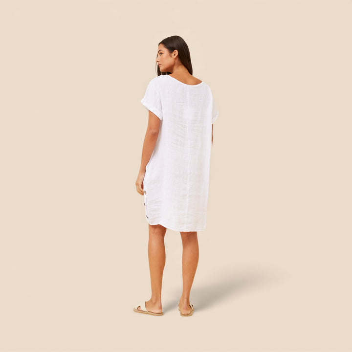 Woman wearing a white linen dress against a beige background