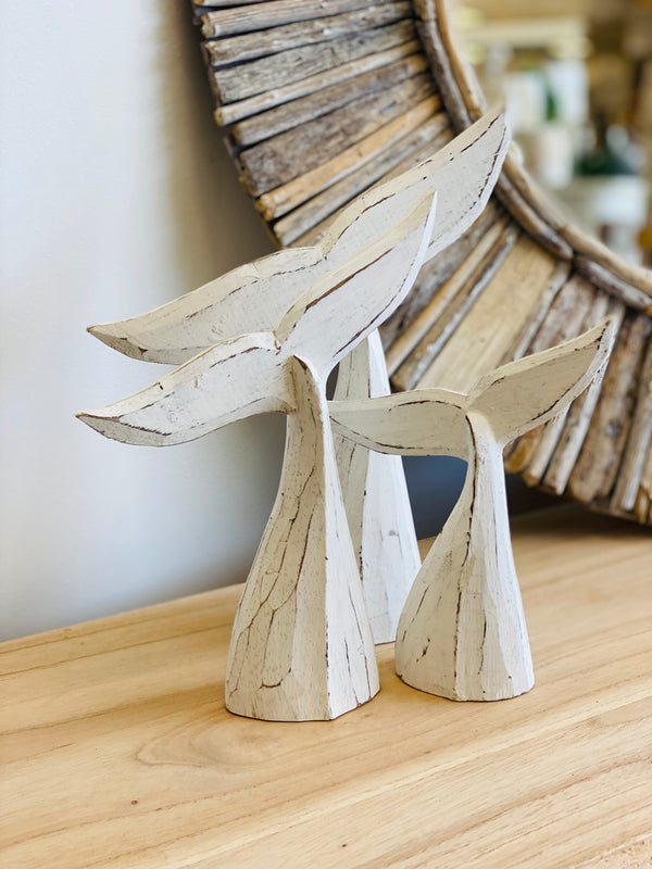 Wooden whale tail sculptures on a wooden surface with a decorative mirror in the background.